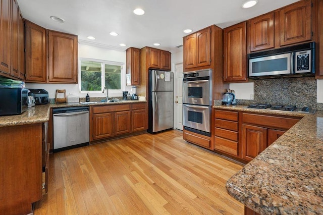 kitchen with sink, tasteful backsplash, light wood-type flooring, stone counters, and stainless steel appliances