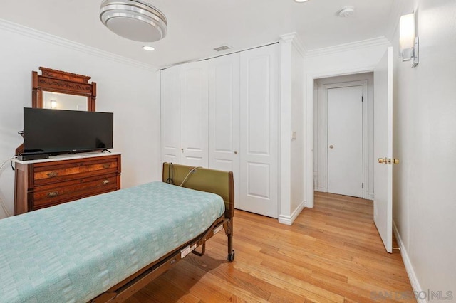 bedroom featuring light hardwood / wood-style flooring, ornamental molding, and a closet