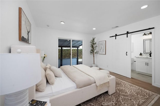 bedroom featuring a barn door, visible vents, wood finished floors, access to exterior, and recessed lighting