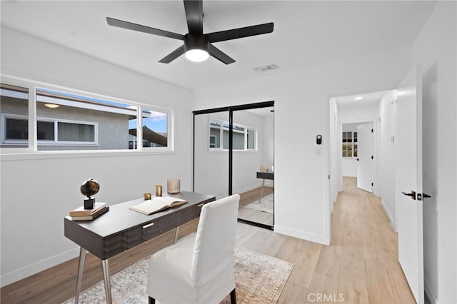 office area with light wood-style flooring, visible vents, ceiling fan, and baseboards