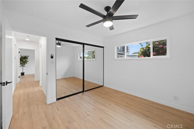 unfurnished bedroom featuring light wood-type flooring, a ceiling fan, baseboards, and a closet