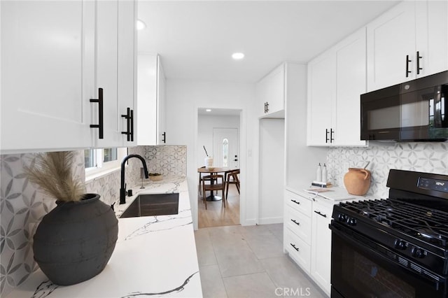 kitchen with light stone countertops, black appliances, white cabinets, and a sink