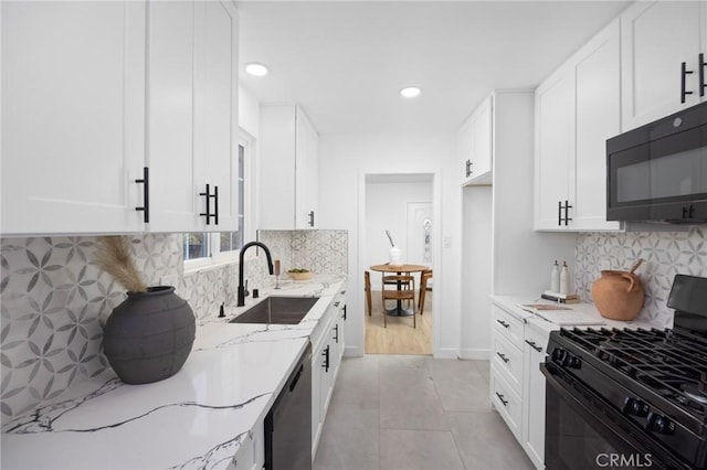 kitchen with light tile patterned floors, light stone counters, a sink, white cabinetry, and black appliances