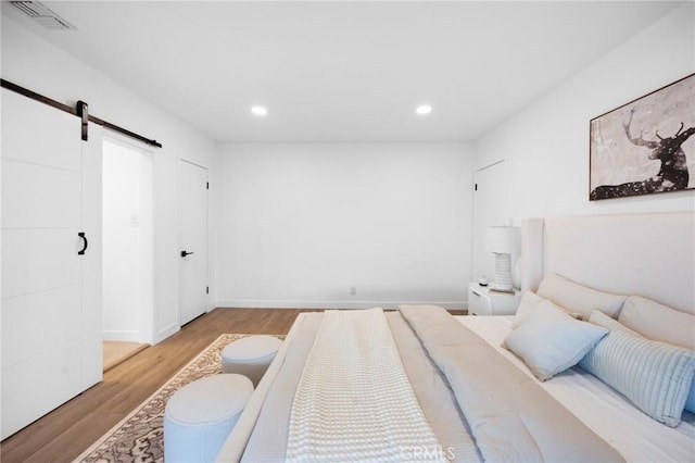 bedroom with a barn door, visible vents, baseboards, light wood-style flooring, and recessed lighting