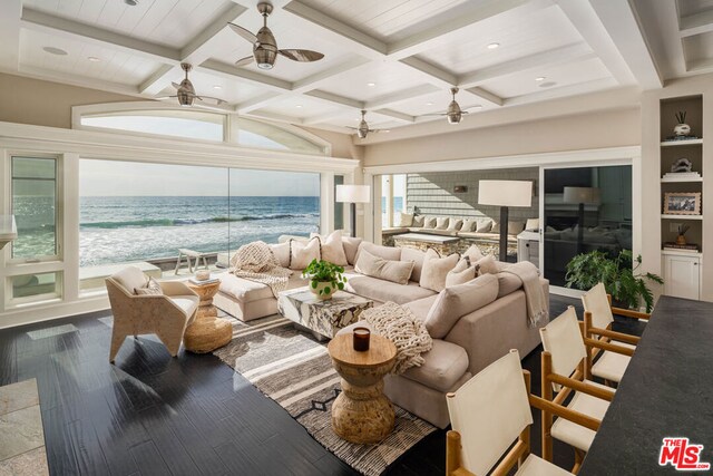 living room featuring ceiling fan, beam ceiling, a beach view, and a water view