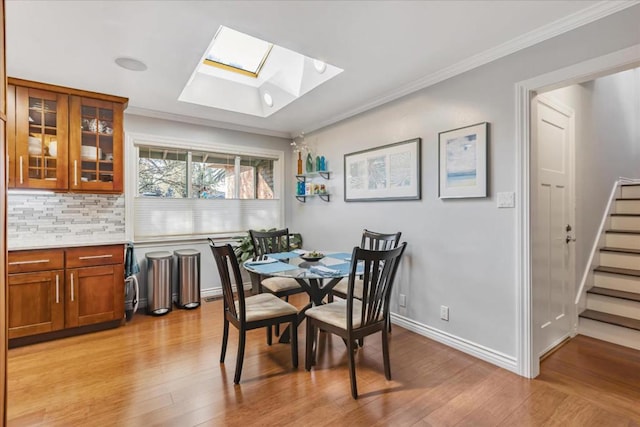 dining space featuring a skylight, light hardwood / wood-style flooring, and ornamental molding