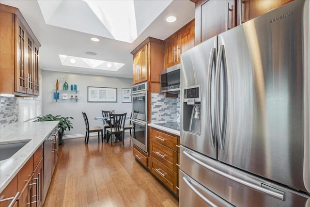 kitchen with light stone counters, tasteful backsplash, a skylight, light hardwood / wood-style flooring, and appliances with stainless steel finishes