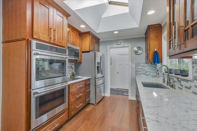 kitchen with sink, tasteful backsplash, appliances with stainless steel finishes, light stone countertops, and light hardwood / wood-style floors