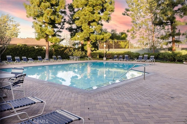pool at dusk featuring a community pool, fence, and a patio