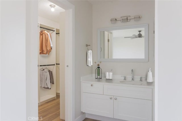 bathroom featuring a spacious closet, wood finished floors, vanity, and a ceiling fan