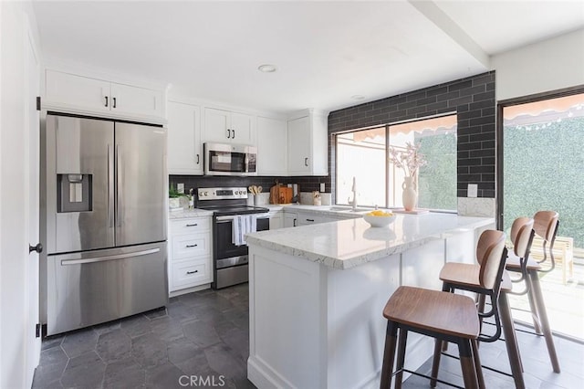 kitchen with a sink, stainless steel appliances, a peninsula, and white cabinetry