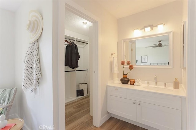 bathroom featuring baseboards, a walk in closet, wood finished floors, and vanity