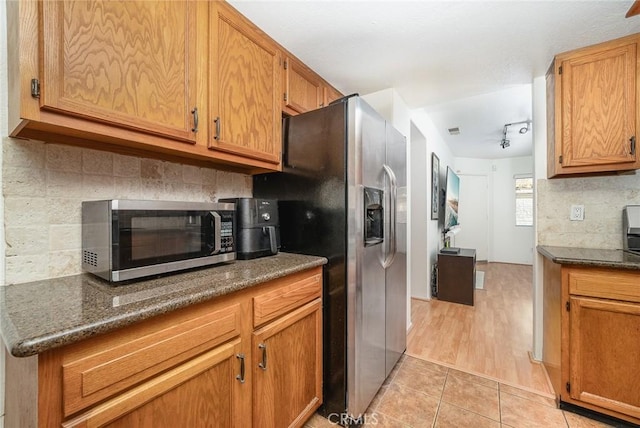 kitchen with stainless steel appliances, dark stone countertops, backsplash, and light tile patterned floors