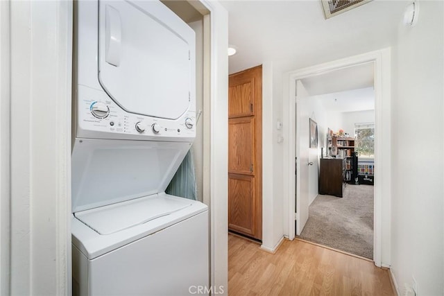 laundry area featuring stacked washer / drying machine and light hardwood / wood-style flooring