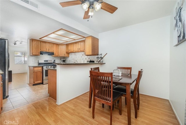 kitchen with appliances with stainless steel finishes, kitchen peninsula, ceiling fan, light hardwood / wood-style floors, and decorative backsplash