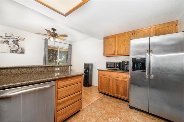 kitchen with dark stone counters, light tile patterned floors, ceiling fan, stainless steel appliances, and decorative backsplash