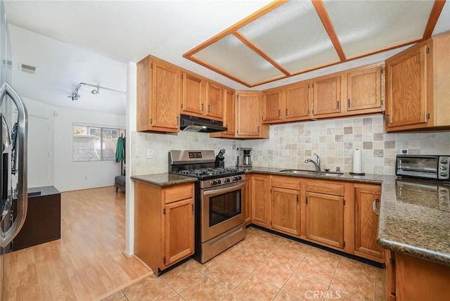 kitchen featuring sink, light tile patterned floors, stainless steel gas range, decorative backsplash, and dark stone counters