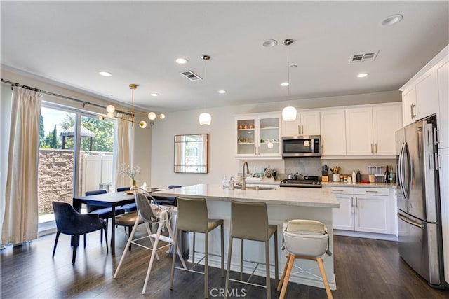 kitchen with sink, appliances with stainless steel finishes, hanging light fixtures, an island with sink, and white cabinets