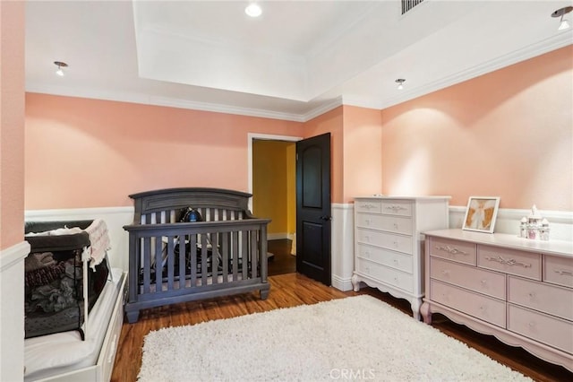 bedroom featuring hardwood / wood-style flooring, ornamental molding, a raised ceiling, and a crib