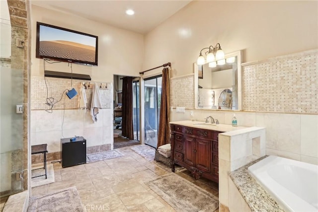 bathroom with vanity, tile walls, and a relaxing tiled tub