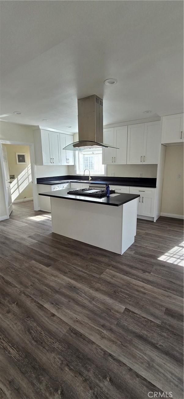 kitchen with island exhaust hood, dark hardwood / wood-style floors, a kitchen island, and white cabinets