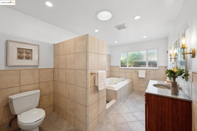 bathroom with tiled tub, tile walls, vanity, tile patterned floors, and toilet