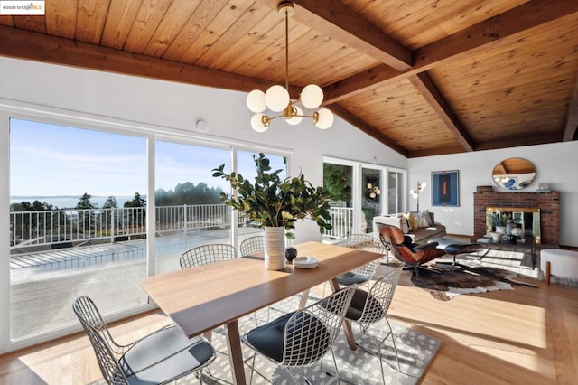 dining area featuring lofted ceiling with beams, hardwood / wood-style flooring, a notable chandelier, wood ceiling, and a brick fireplace