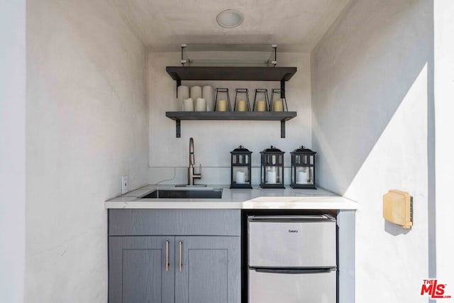 bar with gray cabinetry, sink, and stainless steel refrigerator