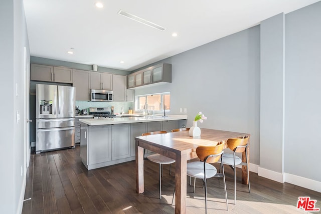 kitchen with gray cabinetry, decorative backsplash, kitchen peninsula, stainless steel appliances, and dark wood-type flooring