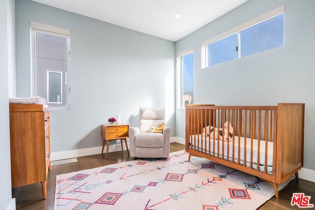 bedroom with a crib and dark wood-type flooring