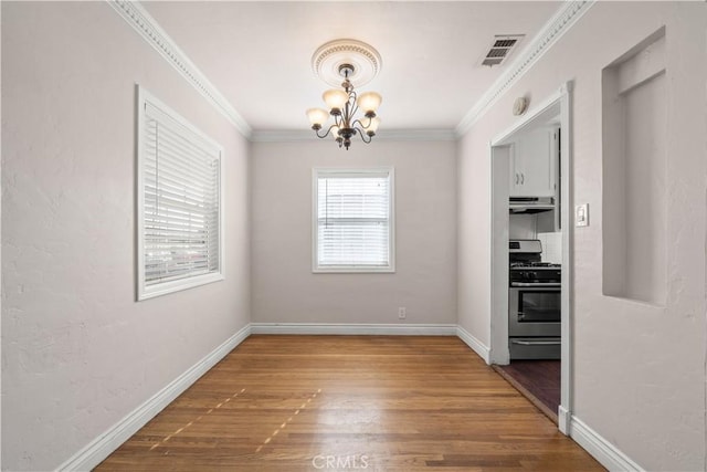 unfurnished dining area featuring dark hardwood / wood-style flooring, crown molding, and an inviting chandelier