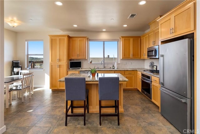 kitchen featuring sink, a center island, appliances with stainless steel finishes, light stone countertops, and backsplash