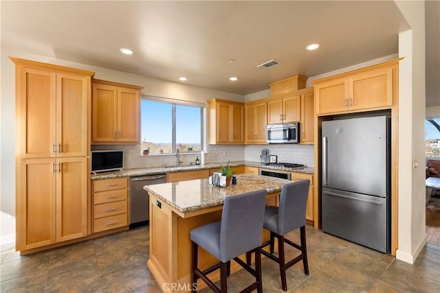 kitchen with sink, a breakfast bar area, a center island, stainless steel appliances, and light stone countertops