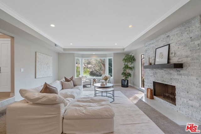 living room featuring crown molding, a tray ceiling, a fireplace, and light colored carpet