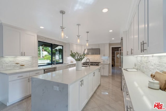 kitchen with pendant lighting, white cabinetry, light stone counters, tasteful backsplash, and a center island with sink