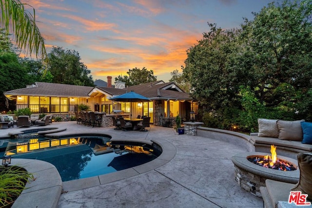 pool at dusk featuring a patio area and an outdoor living space with a fire pit