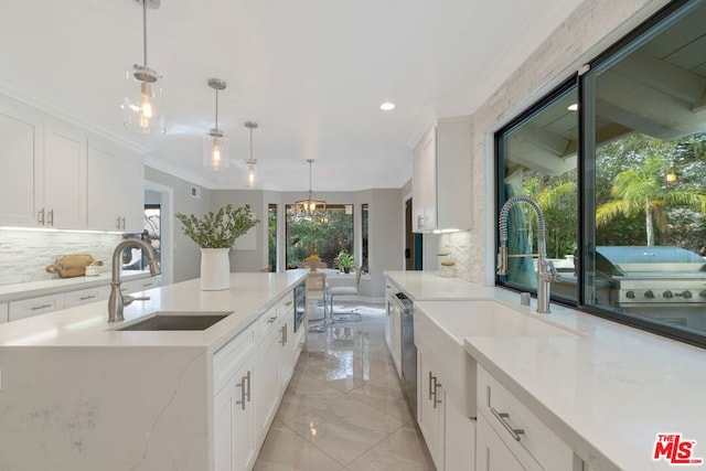 kitchen featuring sink, tasteful backsplash, an island with sink, white cabinets, and decorative light fixtures