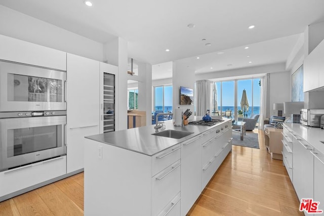 kitchen with sink, appliances with stainless steel finishes, white cabinetry, a center island with sink, and light wood-type flooring