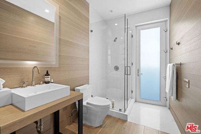 bathroom featuring sink, wooden walls, wood-type flooring, a shower with shower door, and toilet