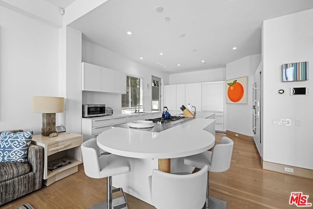 kitchen featuring appliances with stainless steel finishes, sink, a breakfast bar area, white cabinets, and light hardwood / wood-style floors