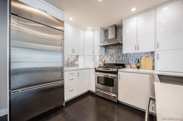 kitchen with appliances with stainless steel finishes, dark hardwood / wood-style floors, wall chimney range hood, decorative backsplash, and white cabinets