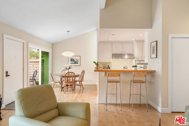 interior space with pendant lighting, white cabinets, a kitchen breakfast bar, light hardwood / wood-style floors, and kitchen peninsula