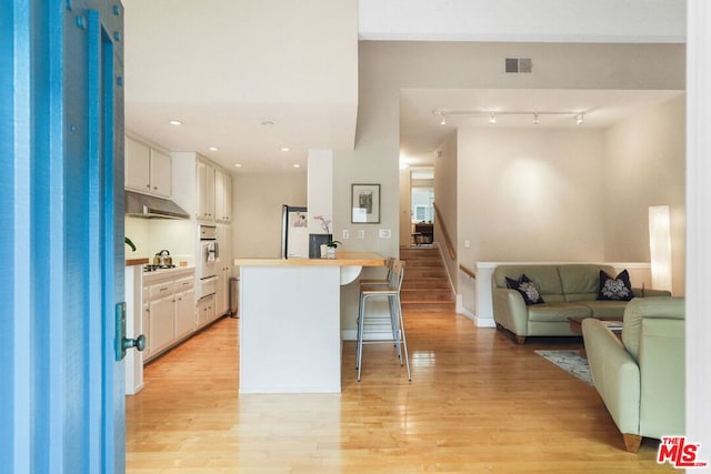 kitchen featuring white appliances, a breakfast bar area, white cabinetry, light hardwood / wood-style floors, and kitchen peninsula