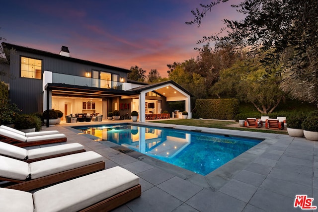 pool at dusk with an outdoor hangout area and a patio