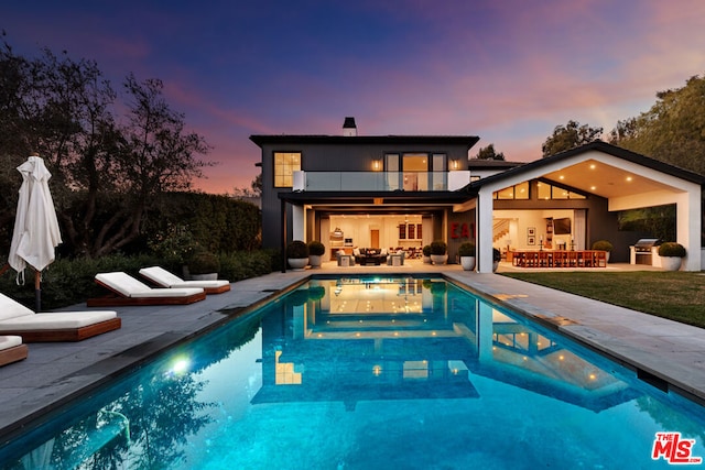 back house at dusk featuring an outdoor living space, a patio, and a balcony