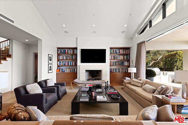 living room featuring built in shelves, high vaulted ceiling, and light hardwood / wood-style floors