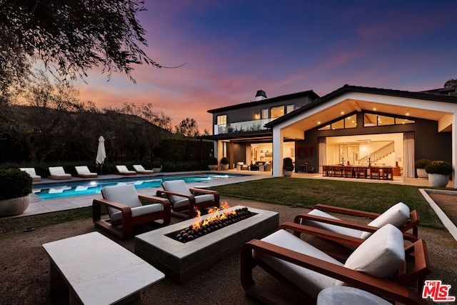 pool at dusk with a patio, a lawn, and a fire pit