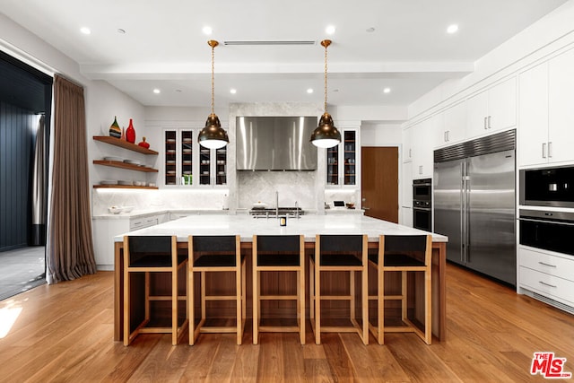 kitchen featuring built in fridge, pendant lighting, a large island, wall chimney range hood, and beam ceiling