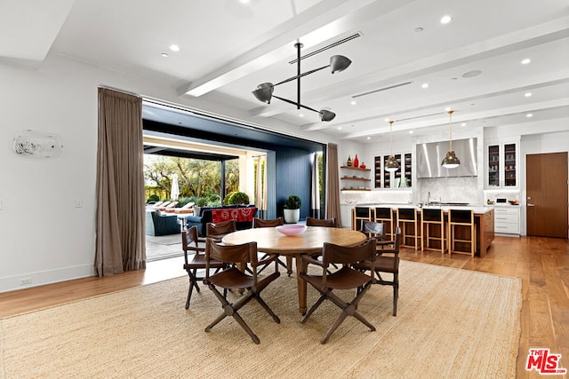 dining area with beam ceiling, light hardwood / wood-style flooring, and indoor bar