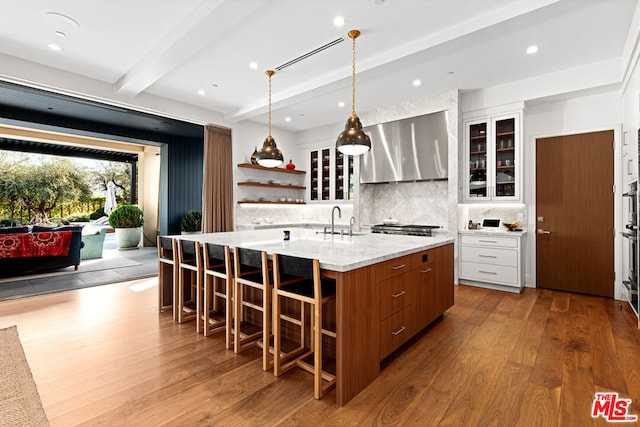 kitchen with beamed ceiling, sink, white cabinets, a center island with sink, and light hardwood / wood-style flooring